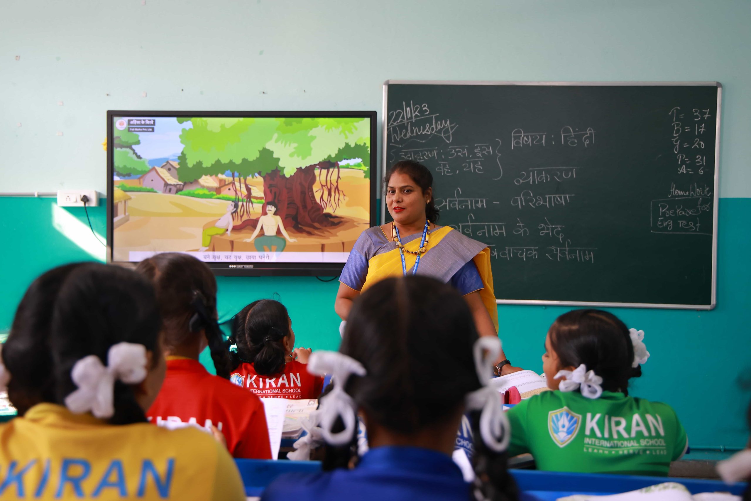 An interactive classroom scene at Kiran International School, with a teacher using aids and a digital board to facilitate engaging and modern teaching methods, enhancing the learning experience for students.