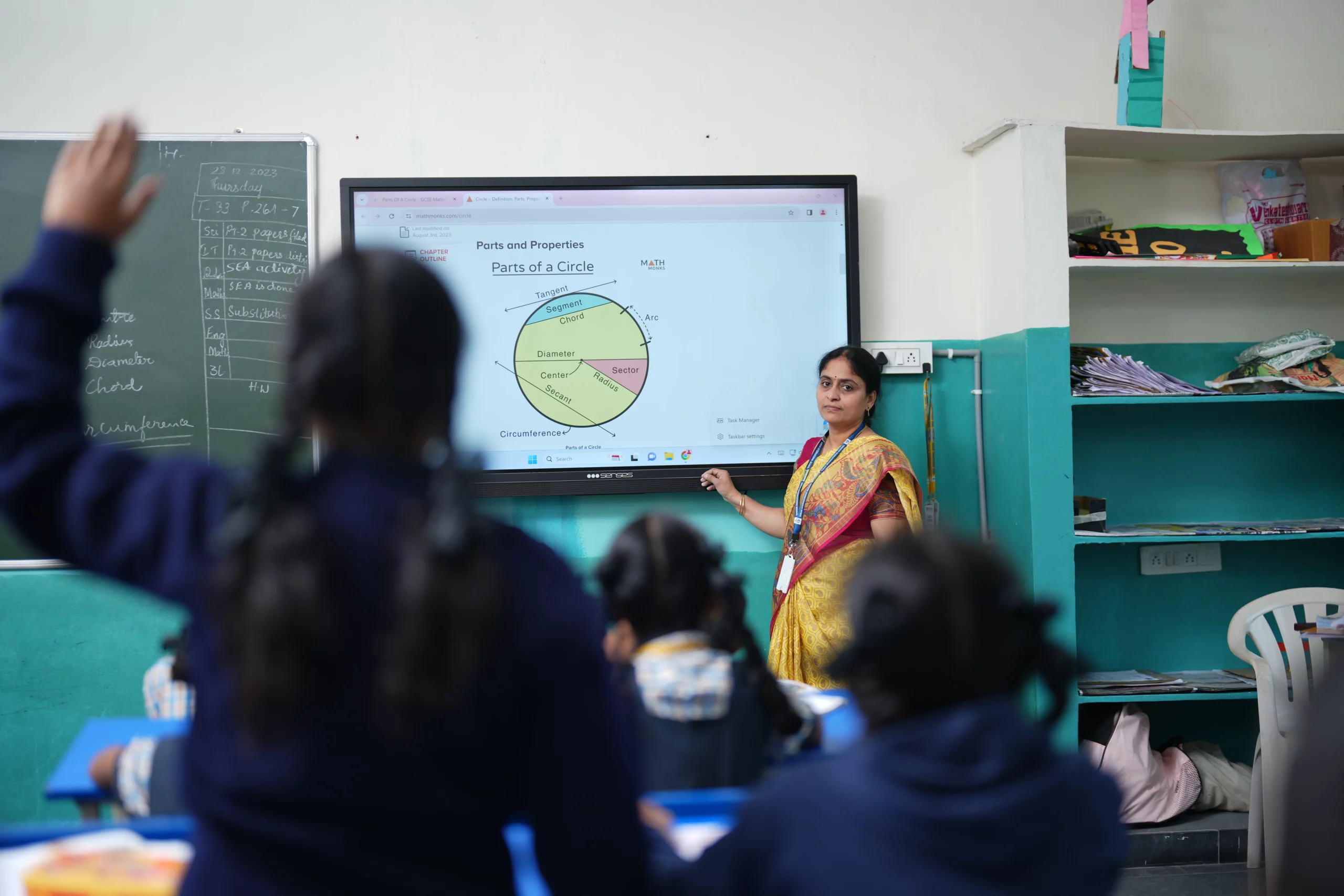 An interactive classroom scene at Kiran International School, with a teacher using aids and a digital board to facilitate engaging and modern teaching methods, enhancing the learning experience for students.
